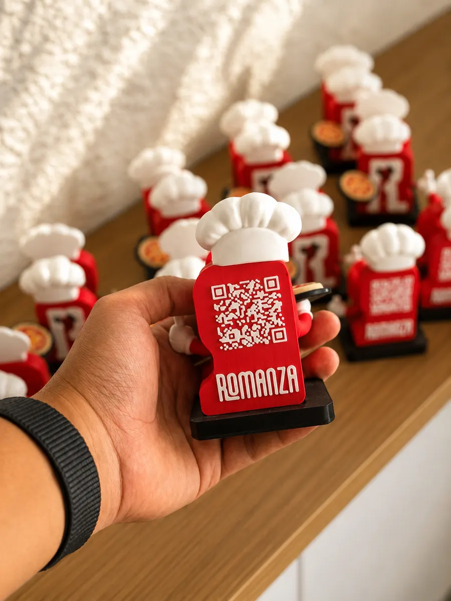 Mano sosteniendo un servilletero de Romanza Pizzería con la mascota y un código QR de la carta